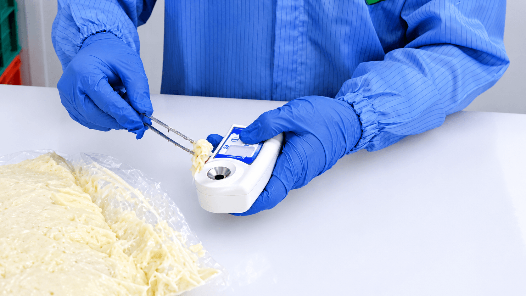 Technician wearing blue gloves tests a small food sample with a handheld digital measuring instrument.