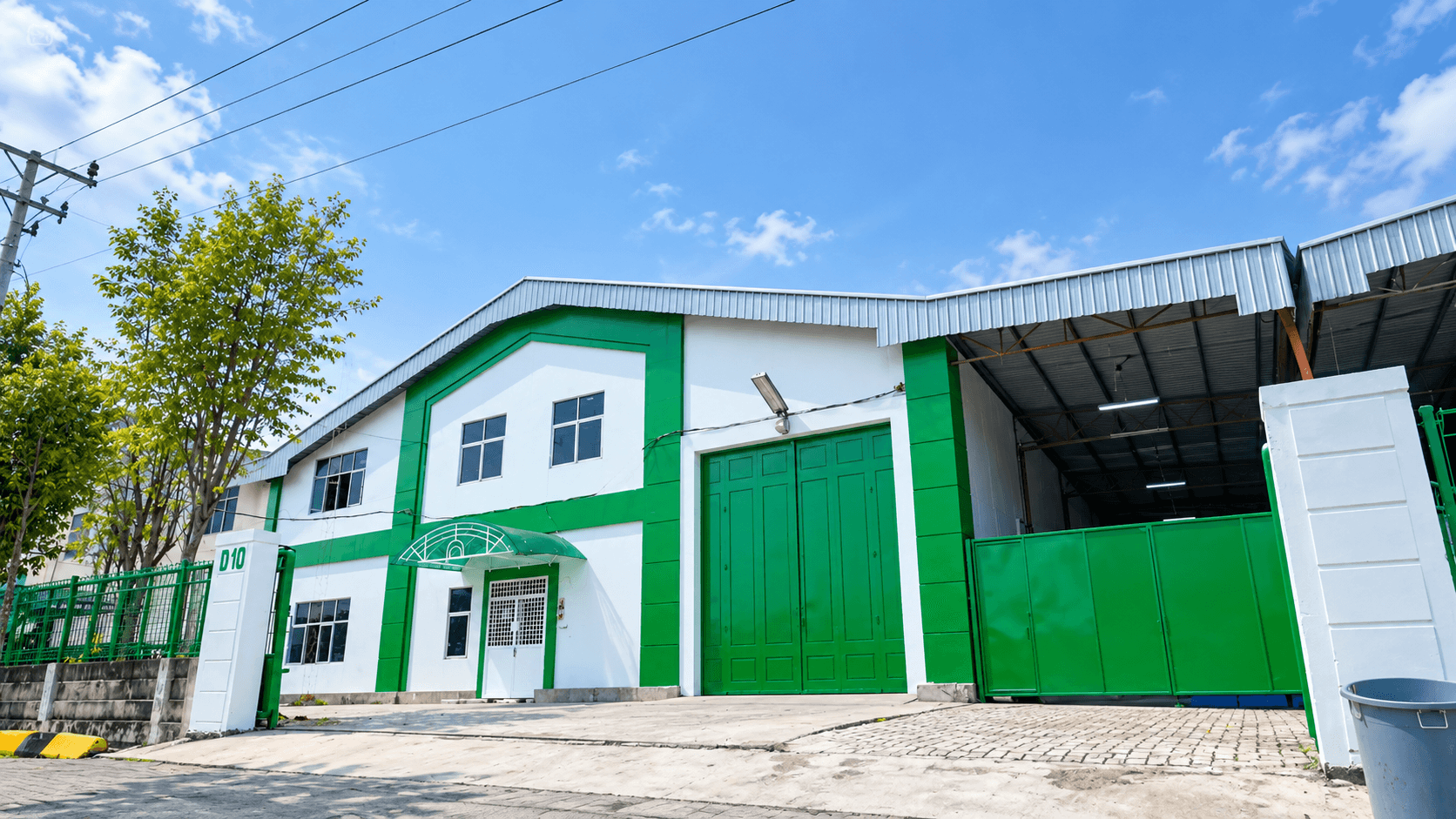Exterior of a white industrial warehouse with green doors and a covered loading area.