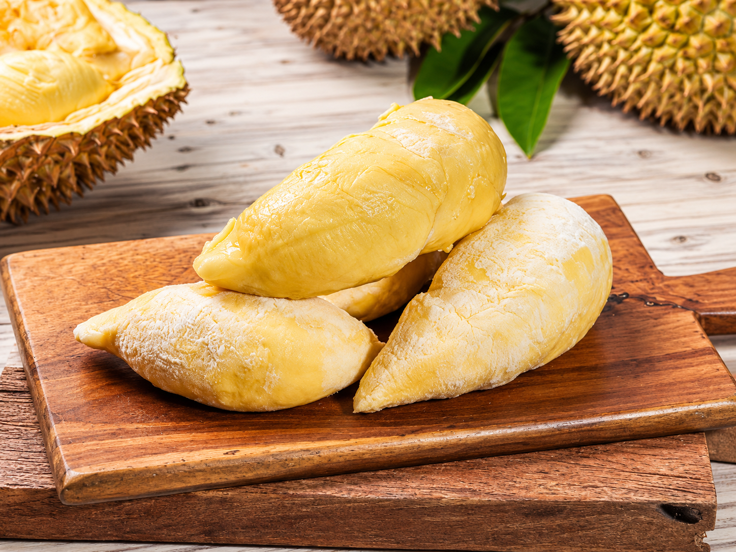Yellow durian flesh segments arranged on a wooden cutting board beside opened durian shells.